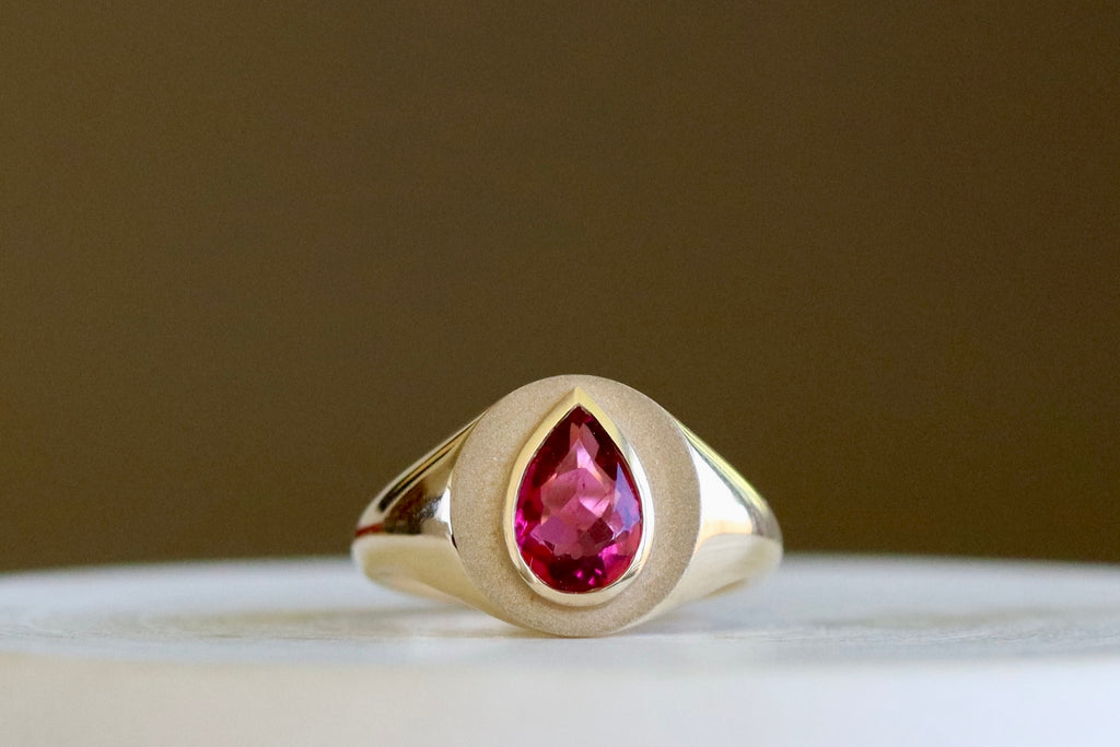 Circle Signet with Pear Tourmaline by Elizabeth Street Jewelry is a multi finish classic circle signet ring with a bezel set rubellite pear tourmaline on a tapered 14k yellow gold band. Handmade in Los Angeles. Size 7.