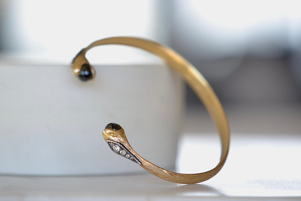 Duo Snake Cuff by Arman Sarkisyan is A single piece of gold is shaped and hammered into a cuff that has snake heads on each end with oxidized silver and diamond detail on each snake and holding a black diamond brio 2.41TCW..