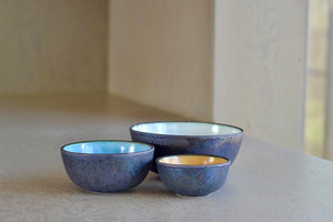 Set of Three (3) stacking bowls by One Kiln. This set of three round ceramic accent bowls has a special outer glaze that is made by mixing in ash from the Sakurajima volcano in Kagoshima. These extra small, small and medium bowls stack beautifully. The colors are ash and white, ash and yellow, and ash and blue. Made in Kagoshima, Japan.