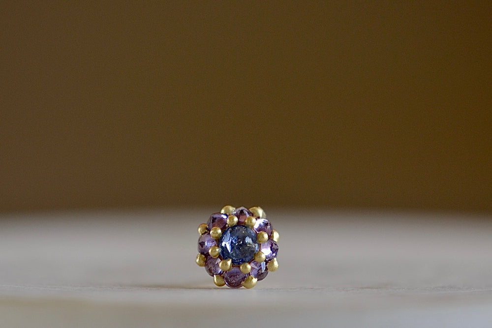 Larkspur stud earring by Polly Wales is a  single earring is a smaller floral cluster made out of a half sphere in gold with a cabochon and encrusted inverted brilliant sapphires. We have one in blue and lavender.
