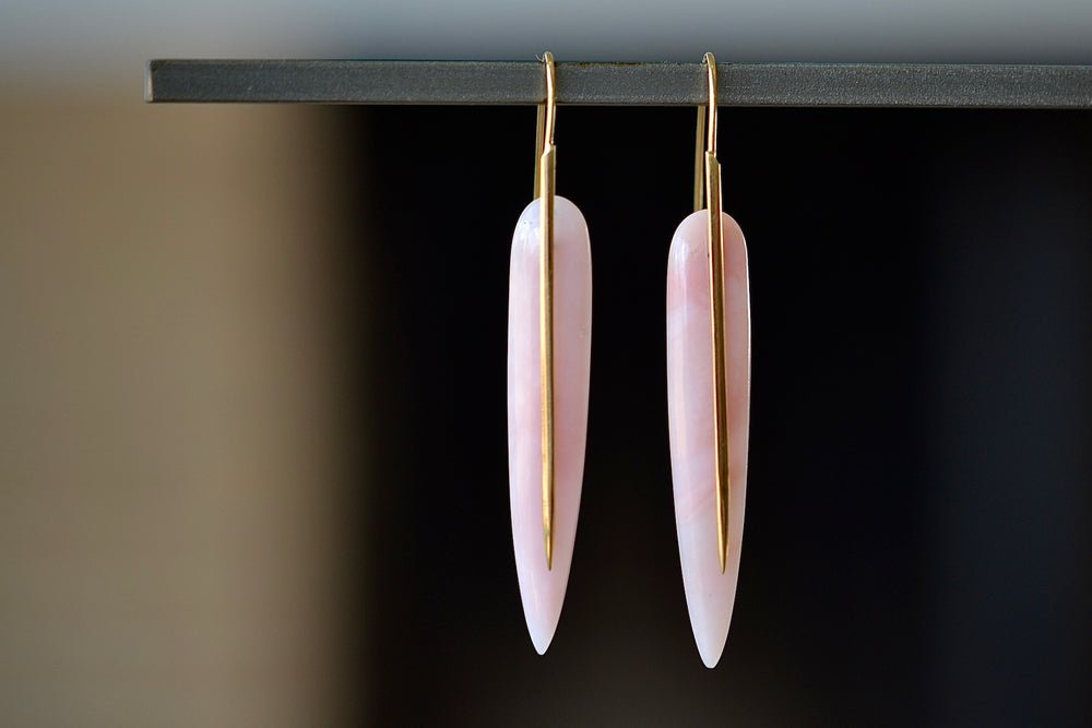 The Rachel Atherley Feather Earrings in Pink Opal are One of a kind articulating and tapered feather shaped slices of pink opal hang on 18k yellow gold ear wire hooks that extend as a sword or spear and form these earrings.