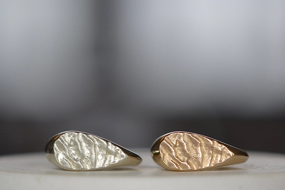 Tidal Teardrop Signet rings in white and yellow gold also known as The 'Tidal 12' is a teardrop shaped and solid modern signet ring in 9k yellow or white gold with polished band and matte face, featuring the maker's signature 'low tide' or 'ripple' texture on the face.
