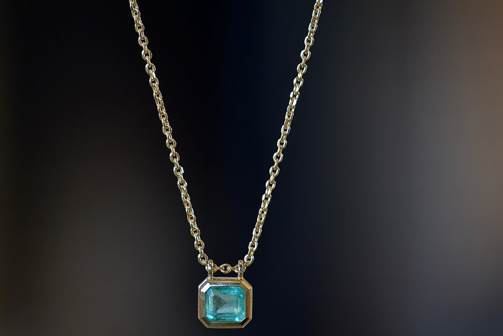 The Duo Bale Emerald Necklace by Elizabeth Street is a bezel set, translucent and almost square shaped Columbian emerald with twin bales and on a 14k yellow gold chain. 