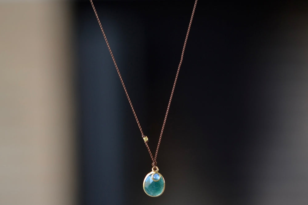 Grandidierite and Sapphire Pendant Necklace designed by Margaret Solow is a A green and faceted Gradidierite stone slice accompanied by a smaller white sapphire slice set in 18k gold with with a gold bead on the string makes this one of a kind organic pendant necklace