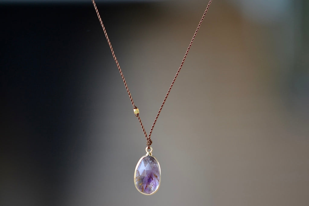 Super 7 Pendant Necklace designed by Margaret Solow is a An Individual faceted, translucent and purple Super 7 crystal slice with natural inclusions set in 14k gold with with a gold bead on the string makes this one of a kind organic pendant necklace.