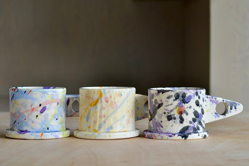 A selection of EXP standard splatter mugs by Peter Shire and Echo Park Pottery. The EXP standard splatter mug is a glazed ceramic mug with a triangular handle, made by utilizing slab construction that is hand rolled. Inspired by the techniques of Adrian Saxe and the paintings of Sam Francis, the mug was designed by Peter Shire for Echo Park Pottery. Peter is one of the original members of the Memphis Group, founded by Ettore Sottsas in Italy. Handmade in Echo Park, Los Angeles.