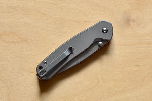 Pyrite Button Lock Titanium Knife is a button lock knife with a titanium handle folded with pocket clip showing.