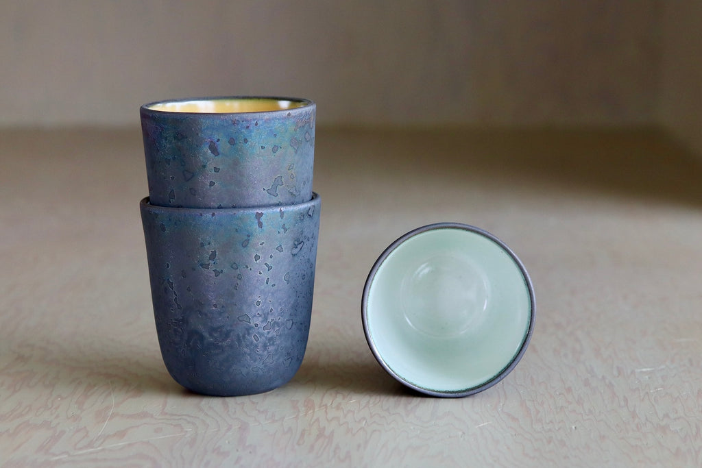 One Kiln Petit Cup  Ash + White next to two stacked mugs.