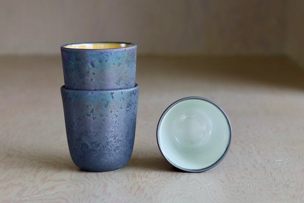 One Kiln Petit Cup  Ash + White next to two stacked mugs.