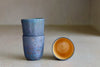 One Kiln Petit Cup Ash + Yellow next to two stacked cups.