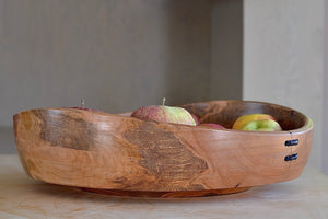 Apples sticking out of the Circle Factory bowl in Maple by Geoarge Peterson is a blonde wood apple bowl with repairs deatail.