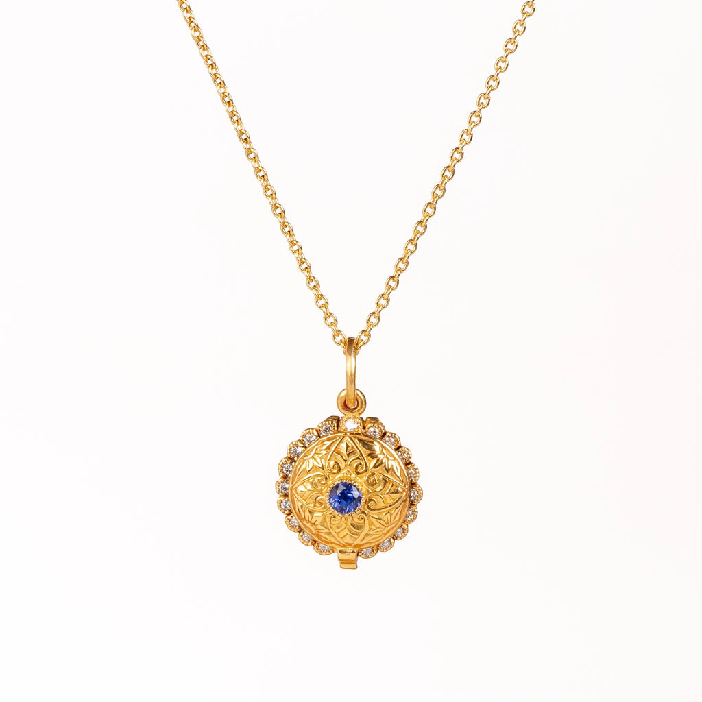 Mini Lace Locket by Arman Sarkisyan is a miniature scale locket in 22k gold with a blue sapphire center stone and lace like edging with white diamond accents hangs on a beautiful 18k gold chain. Detailed engraving on the back of locket which opens. Handmade in California.