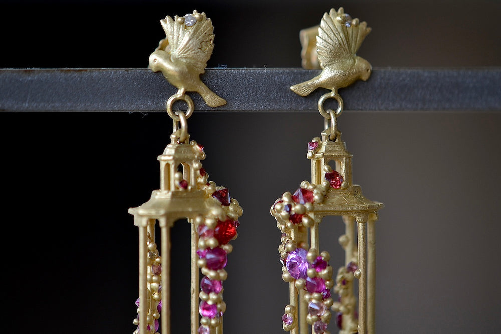 Close up detail of Polly Wales Jade Terrace Pagoda Earrings 18K yellow recycled gold pagoda forms hanging from a bird stud encrusted with a pearl pink and orange sapphire sapphires. Cast not set.