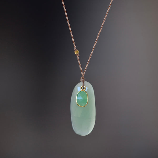 Chrysoprase and Sapphire Pendant Necklace by Margaret Solow is an organic necklace consisting of a smaller and bezel set green sapphire on top of a larger oval pale green raw chrysoprase that hangs on a cord with an 18k gold bead and has a clasp closure.