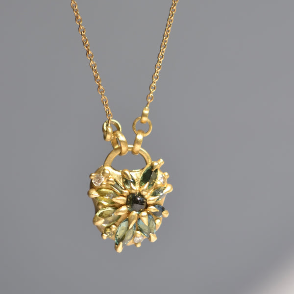 Green Fantaisie Encrusted Padlock Necklace by Polly Wales is a padlock in 18K yellow gold and encrusted with mixed green sapphires, a center cabochon and an accent diamond hanging on a chain that attaches to the lock handle by pulling the lever. Recycled gold. Cast in Place. Cast not set. 