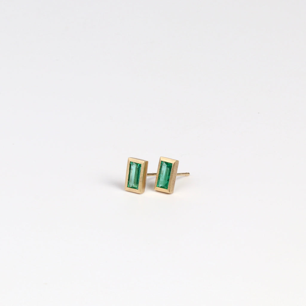 Side view of Elongated Emerald stud earrings with Zambian stone and bezel set in satin finish 14k yellow gold with post closure.
