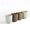 A set of four (4) Japanese ceramic mugs on white background in blue, brown and greenish blue.