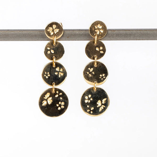 Falling Petal Dot Drops earrings by Kaylin Hertel on white background. These are one each of graduated round discs from xs extra small, to small, medium and extra large on post closure in 14k yellow gold with her signature petal pattern.