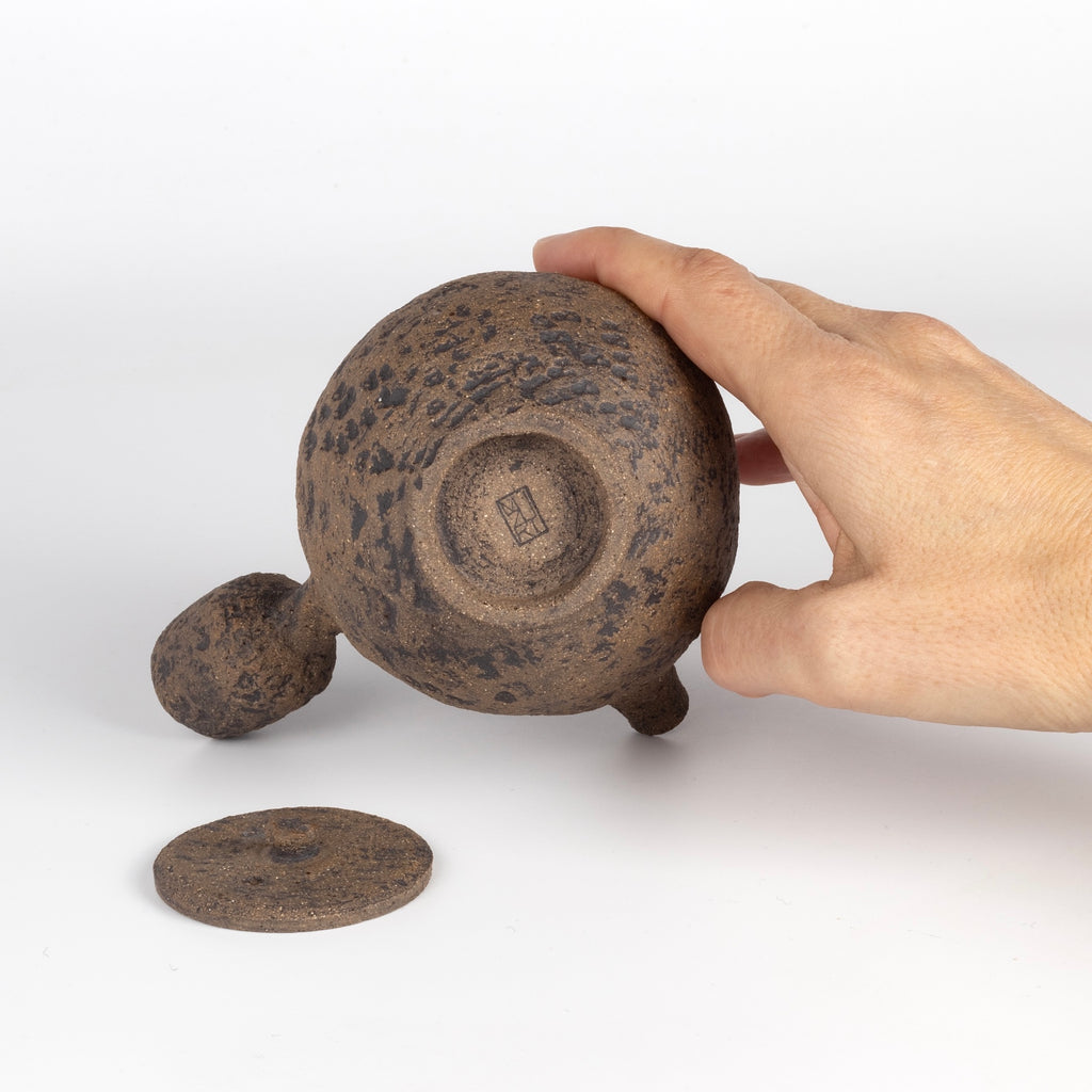 Stamp on bottom of Kyusu Ceramic teapot in brown from Muzuri Ware with lid on the side.