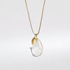 The Coconut Pendant with Seed Charm Necklace in Crystal  designed by Pippa Small is a One clear, transparent and smooth crystal stone with natural inclusions is drilled and hooked on to a gold loop, and accompanied by a bead in 18k yellow gold on a 24" golden waxed cotton cord form this necklace.