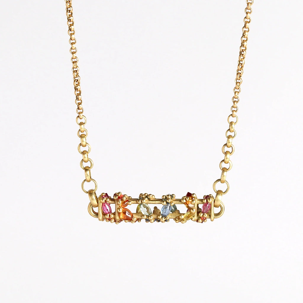 Horizontal Fontaine Bar Necklace in Rainbow by Polly Wales is An oval and three dimensional bar in 18K yellow gold holds a vine of encrusted and inverted rainbow sapphires in pink, fuchsia, blue, yellow, green and red that have been cast and are accompanied by matte gold dots. Recycled Gold. Cast Not Set. Handmade in Los Angeles.