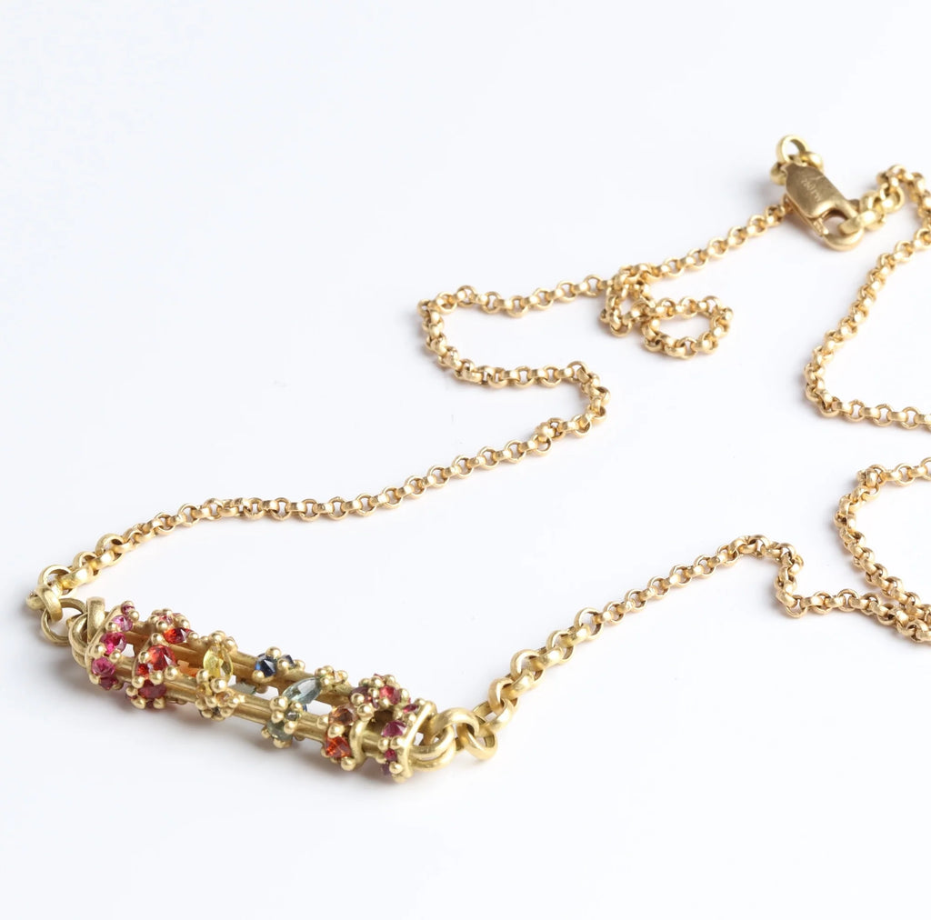 Horizontal Fontaine Bar Necklace in Rainbow by Polly Wales is An oval and three dimensional bar in 18K yellow gold holds a vine of encrusted and inverted rainbow sapphires in pink, fuchsia, blue, yellow, green and red that have been cast and are accompanied by matte gold dots. Recycled Gold. Cast Not Set. Handmade in Los Angeles.