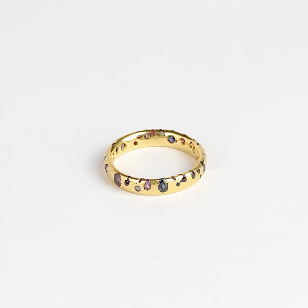 The Purple and Blue Sapphire Band Ring by Polly Wales is a narrow 18k yellow gold band with speckled purple, pink, blue to navy and black sapphires around the circumference for a beautiful confetti-like appearance. Recycled gold. Cast not set.