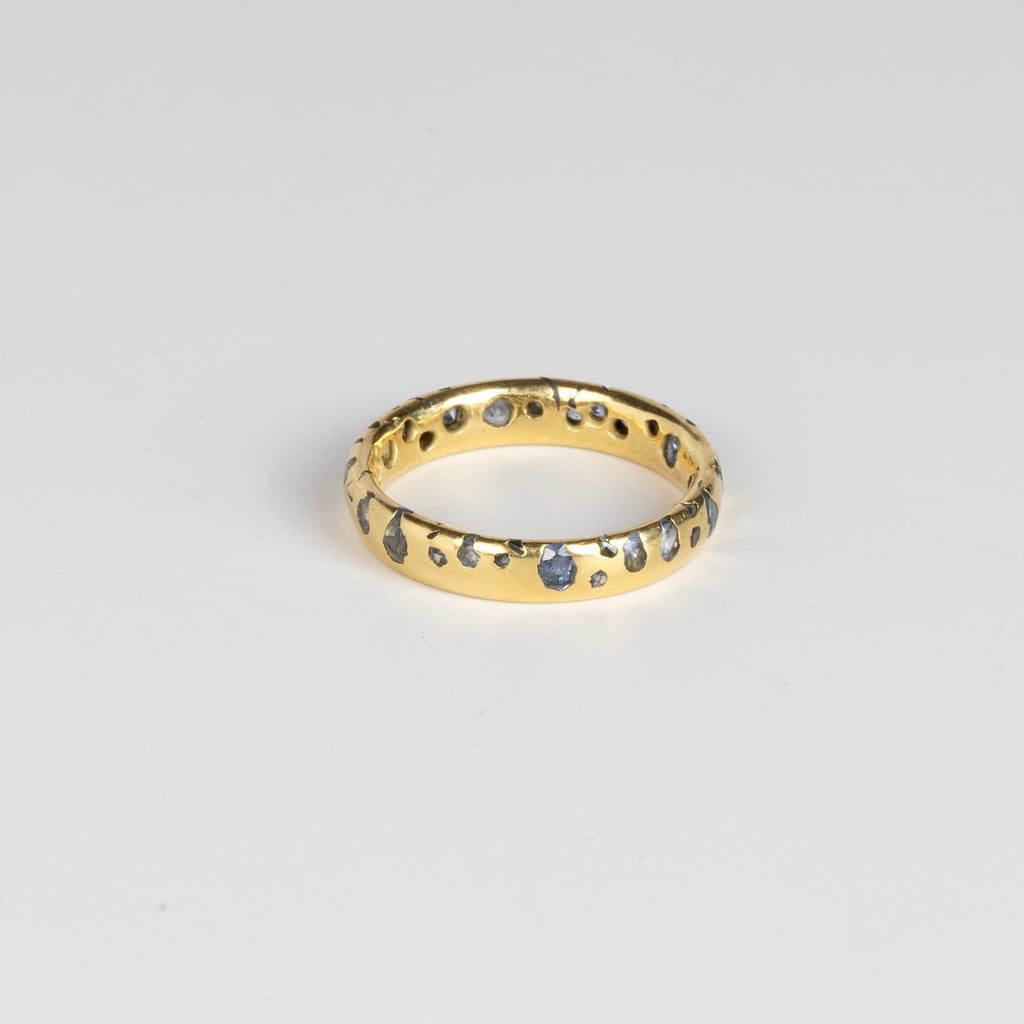 The Cornflower Blue Sapphire Confetti Band designed by Polly Wales is a narrow 18k yellow recycled gold wedding band/ring with speckled ombre light blue sapphires around the circumference. It is cast not set and handmade in Los Angeles.