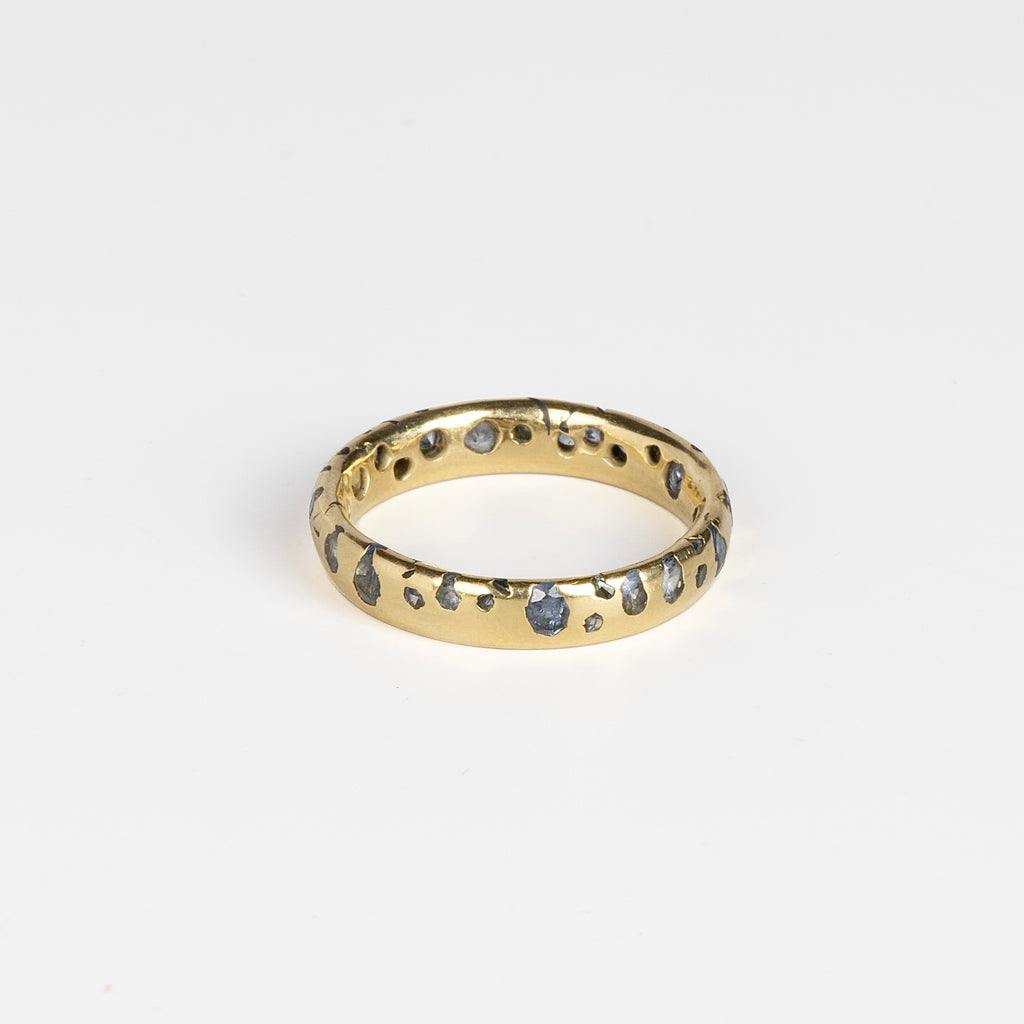 The Cornflower Blue Sapphire Confetti Band designed by Polly Wales is a narrow 18k yellow recycled gold wedding band/ring with speckled ombre light blue sapphires around the circumference. It is cast not set and handmade in Los Angeles.