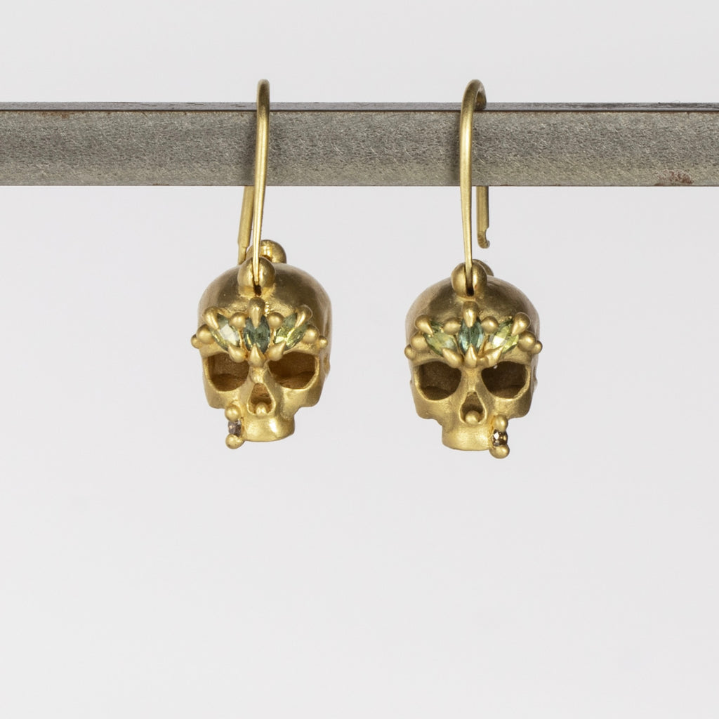 Green Enchanted Skull Safety Pin Earrings by Polly Wales are a pair of safety pin earrings in 18k gold with skulls that have been encrusted with green sapphires and diamonds. Recycled gold. Handcrafted in Los Angeles