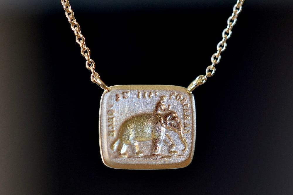 A rectangular disc in gold with satin finish that will turn shiny over time features an image of&nbsp;a man&nbsp;riding an elephant with the French motto "La raison fait ma force" (‘Reason is my strength.’) The elephant is a symbol of wisdom and courage.