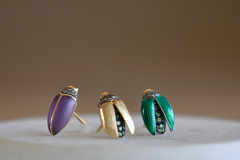 Scarab studs stud earrings by Bibi Van Der Velden are sculptures/ made in 18k gold with a sterling belly and a stone or wings and stones. Starting from left is an amethysst then a gold with tsavorite and enamel with tsavorite.