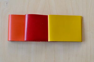 Simple Flap wallets in orange, red and yellow from architect Alice Park shown folded.