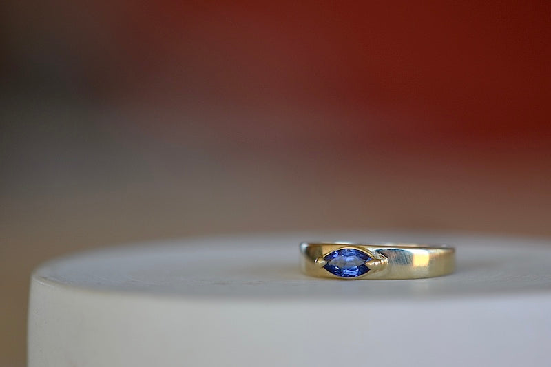 Stoned Slim Cigar Band in Blue Sapphire size 6.5 by Elizabeth street is a marquise cut sapphire in a two prong eagle claw bezel setting on a 14k yellow gold band. .