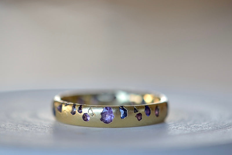 The Purple and Blue Sapphire Band Ring by Polly Wales is a narrow 18k yellow gold band with speckled purple, pink, blue to navy and black sapphires around the circumference for a beautiful confetti-like appearance. Recycled gold. Cast not set.
