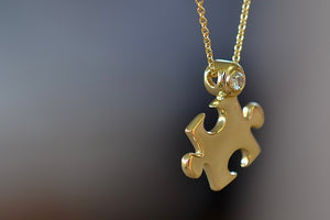 Mini Impetus Puzzle Piece Pendant by Retrouvai is a high polish puzzle piece in gold, accented with one white diamond hangs on a chain. Handcrafted in Los Angeles.
