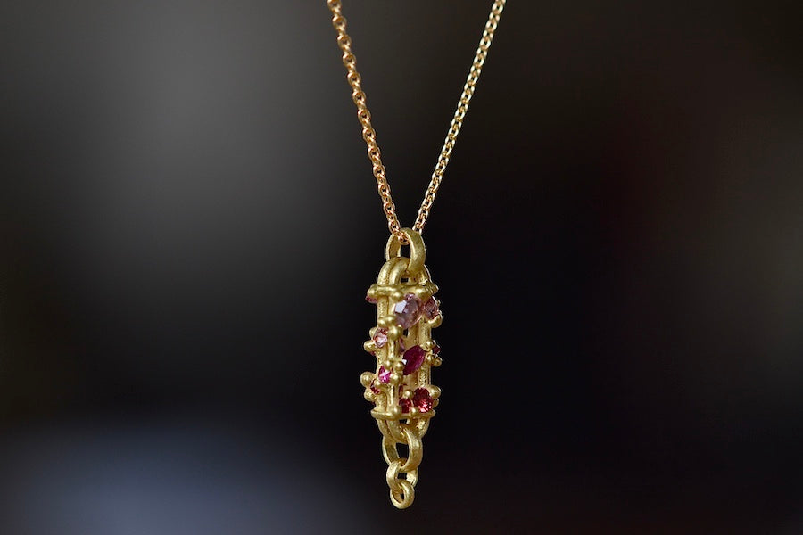 Side view of Vertical Fontaine Bar Necklace in Plum Blossom by Polly Wales is An oval and three dimensional bar in 18K yellow gold holds a vine of encrusted and inverted sapphires in pink, fuchsia and red that have been cast and are accompanied by matte gold dots. The bar hangs on a beautiful gold chain and bale.