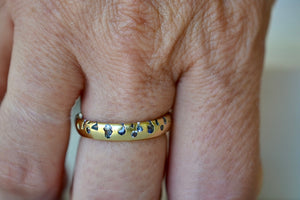 The Cornflower Blue Sapphire Confetti Band designed by Polly Wales is a narrow 18k yellow recycled gold wedding band/ring with speckled ombre light blue sapphires around the circumference. It is cast not set and handmade in Los Angeles.