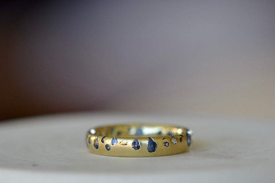 The Cornflower Blue Sapphire Confetti Band designed by Polly Wales is a narrow 18k yellow recycled gold wedding band/ring with speckled ombre light blue sapphires around the circumference. It is cast not set and handmade in Los Angeles.