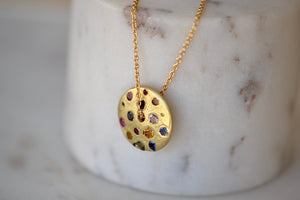 Polly Wales Spinning Disc Pendant Necklace in 18K yellow gold with scattered rainbow sapphires in orange, yellow, pink, blue, purple and lilac hangs on a beautiful chain 22" cast in place and cast not set in recycled gold.