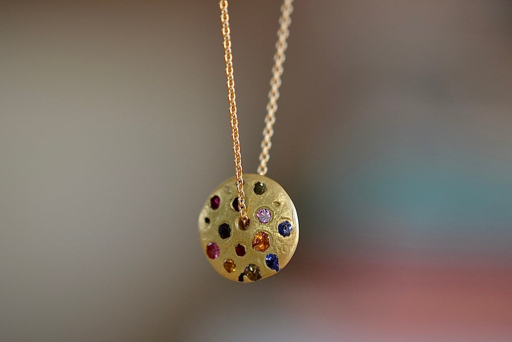 Polly Wales Spinning Disc Pendant Necklace in 18K yellow gold with scattered rainbow sapphires in orange, yellow, pink, blue, purple and lilac hangs on a beautiful chain 22" cast in place and cast not set in recycled gold. 