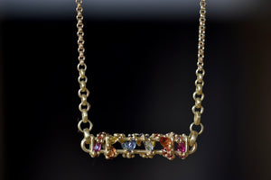 Back view of Horizontal Fontaine Bar Necklace in Rainbow by Polly Wales is An oval and three dimensional bar in 18K yellow gold holds a vine of encrusted and inverted rainbow sapphires in pink, fuchsia, blue, yellow, green and red that have been cast and are accompanied by matte gold dots. Recycled Gold. Cast Not Set. Handmade in Los Angeles.